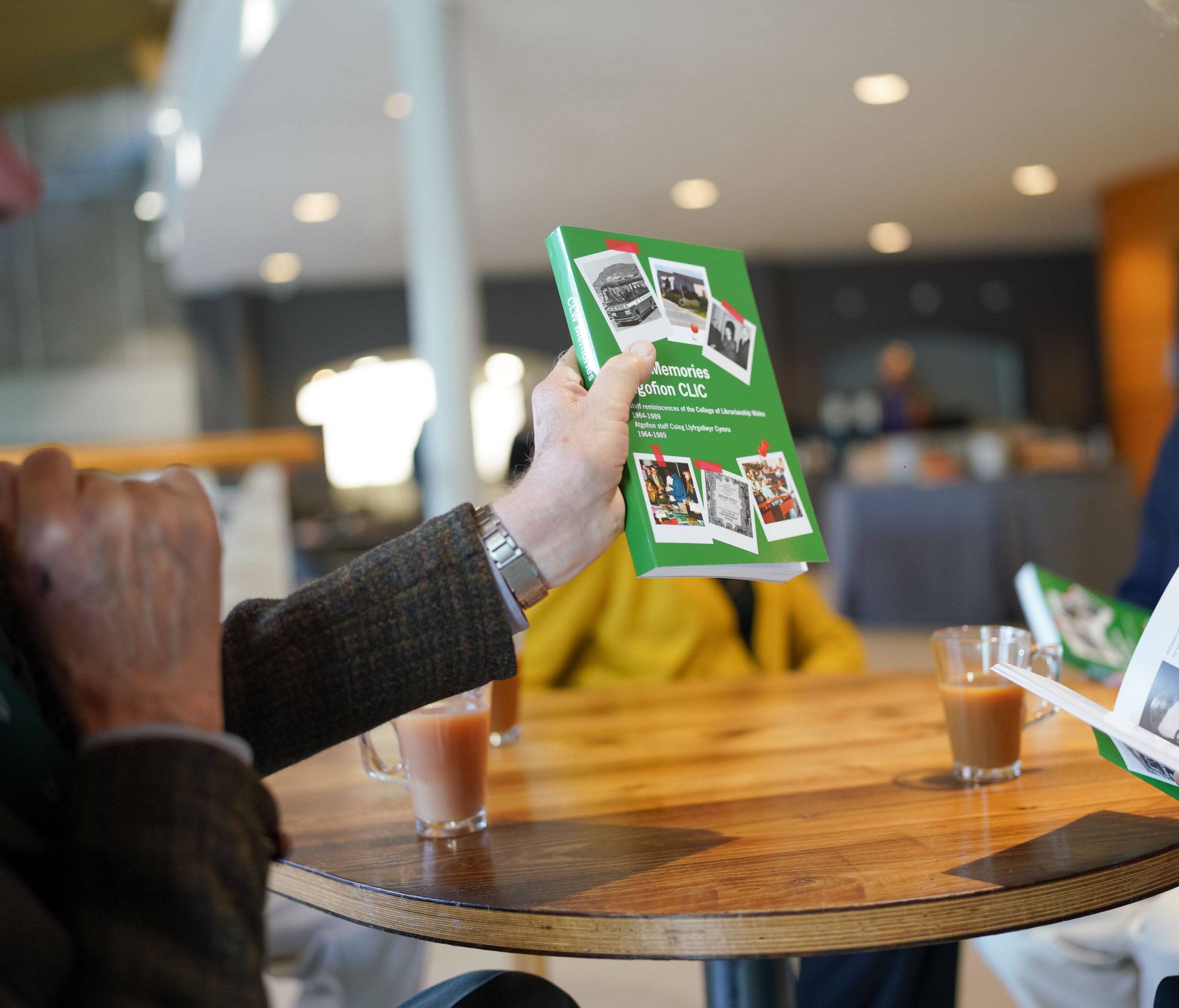 Person holding CLW Memories book and showing cover to someone